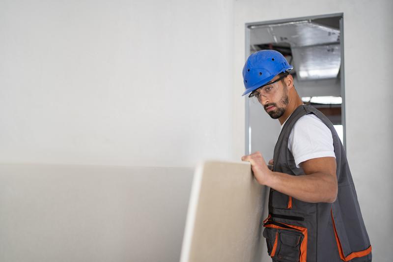 Profissional instalando placa de drywall em obra interna, destacando a diferença entre drywall e gesso.